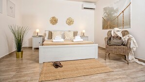 A bedroom with a bed, bedside tables, a potted plant, a wicker chair, and a wall-mounted air conditioner. - Ortigia Boutique Terrace Apt (Siracusa)