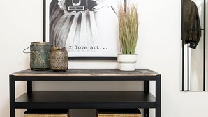 A black metal console table with two wicker baskets, a potted plant, and a framed artwork on the wall. - Ortigia Boutique Terrace Apt (Siracusa)