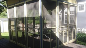 A covered patio area with a screened enclosure, a wooden deck, and outdoor furniture. - Harbor Haven: A Summer Getaway Just Steps from Lake Michigan (Union Pier)