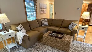 A living room with a sectional sofa, a small side table, a lamp, and a woven ottoman. - Harbor Haven: A Summer Getaway Just Steps from Lake Michigan (Union Pier)