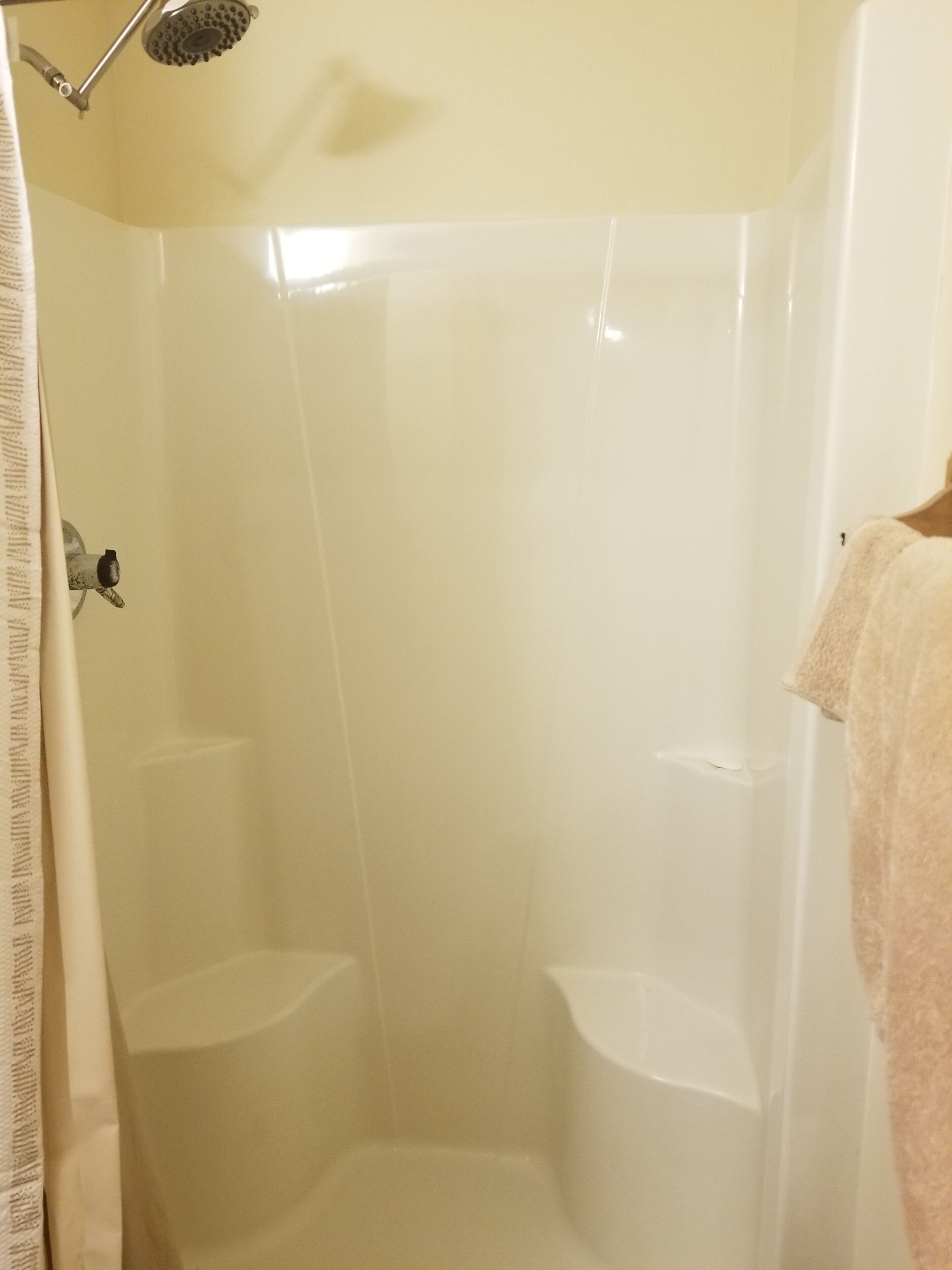 Un box de ducha con pared de azulejos blancos y cabezal de ducha.