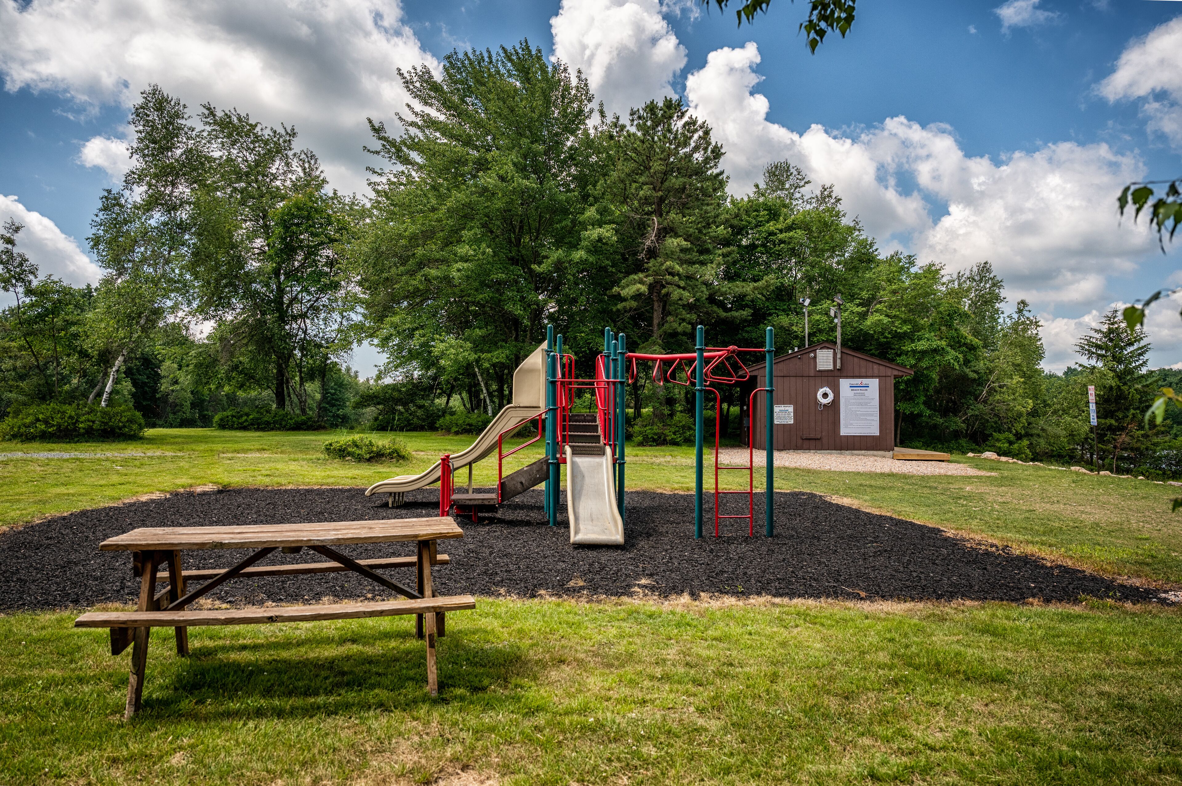 A playground with a slide, swings, and a picnic table in a park.