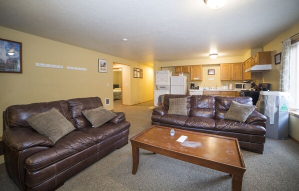 A living room with two brown leather sofas, a wooden coffee table, and a kitchen in the background.