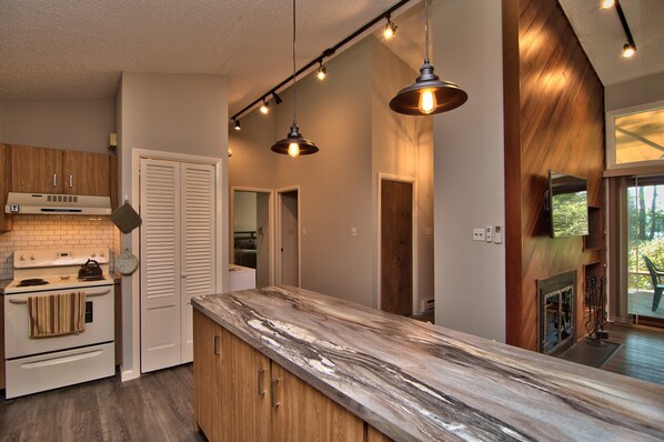 A modern kitchen with a marble countertop, wooden cabinets, a built-in oven, and pendant lighting.
