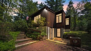 A modern two-story house with a wooden exterior, a flag, and a well-maintained garden. - DOCKSIDE DAYS-LAKEFRONT in Lake Naomi!  Boating, Sunsets and Year-Round Fun (Pocono Pines)