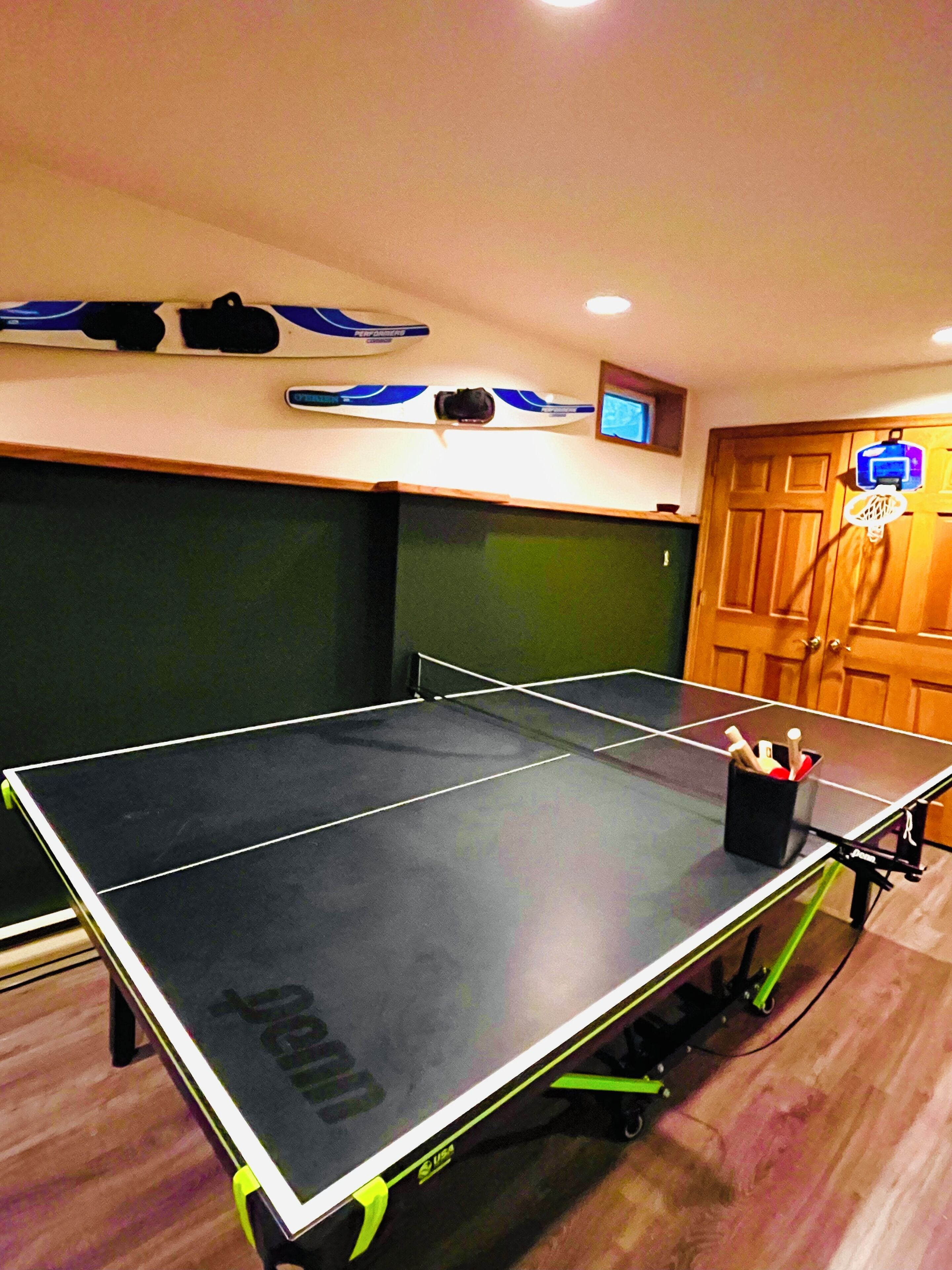 A ping pong table with a black and green table, a black table stand, and a black cup with pens on the table.