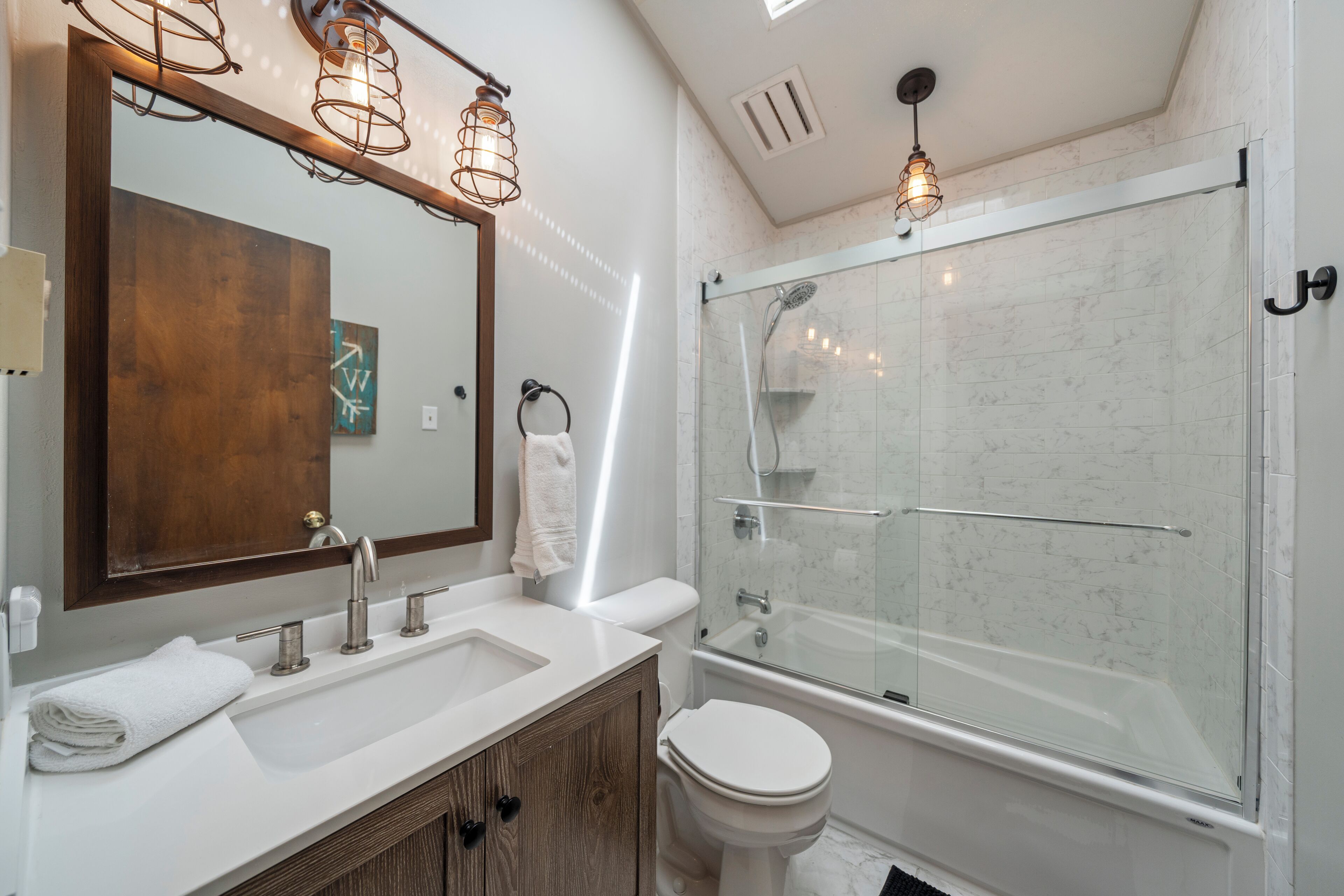 A modern bathroom with a large mirror, two sinks, a toilet, and a glass-enclosed shower.