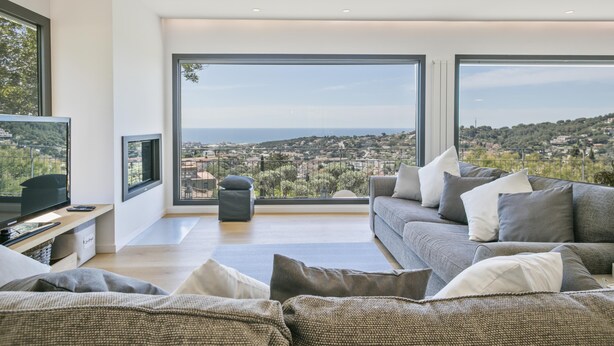 Ein modernes Wohnzimmer mit großem Fenster und Blick auf die Stadt, einer bequemen Couch und einem Flachbildfernseher.
