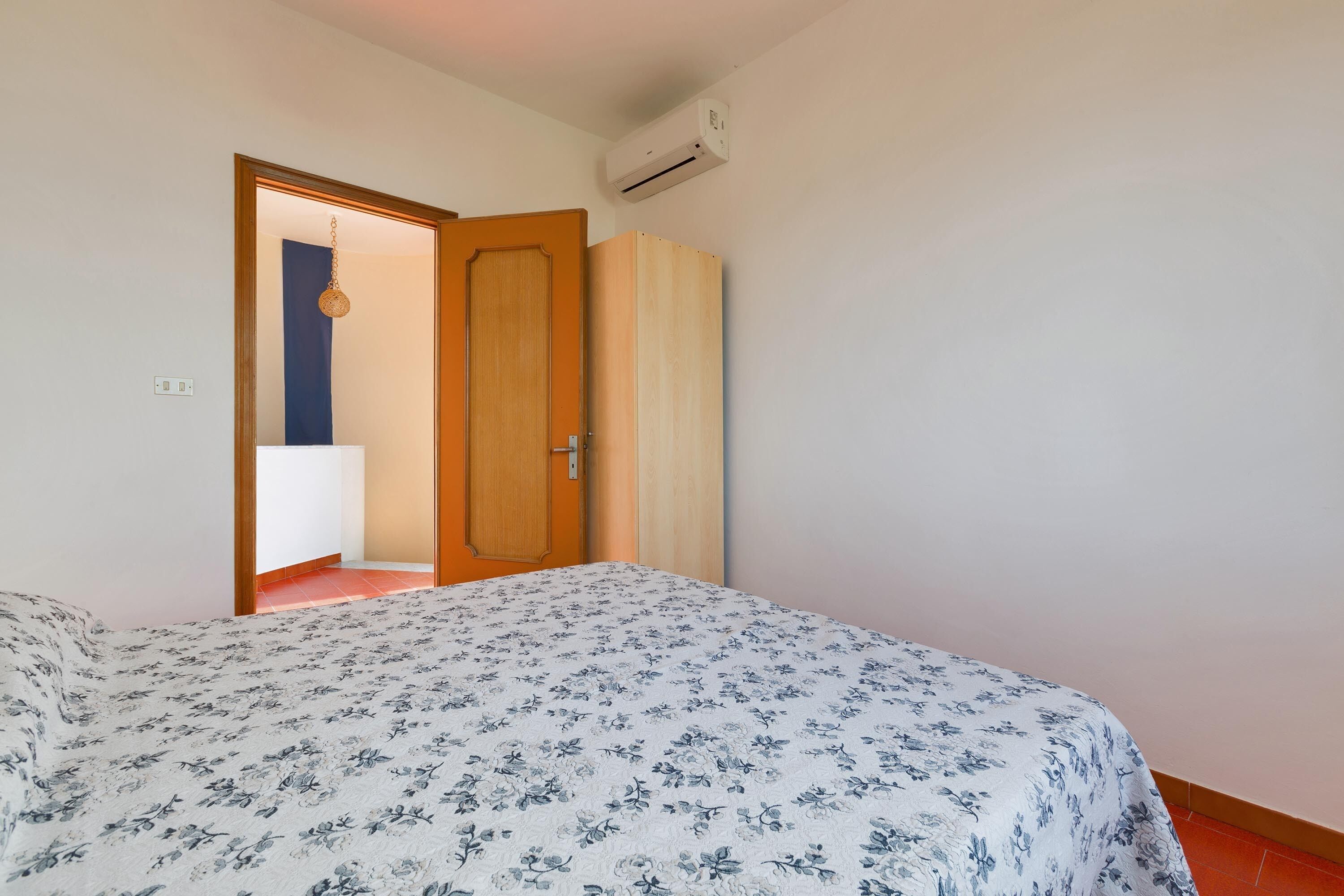 Een slaapkamer met een bed, een kledingkast, een airconditioning en een deur naar een andere kamer.