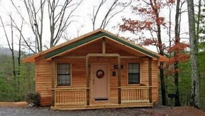 Una pequeña cabaña de madera con un porche, una puerta principal y dos ventanas en la fachada.