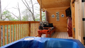 Una terraza de madera con un jacuzzi azul, un banco de madera con cojín floral y un muro de madera con dos adornos de flores.