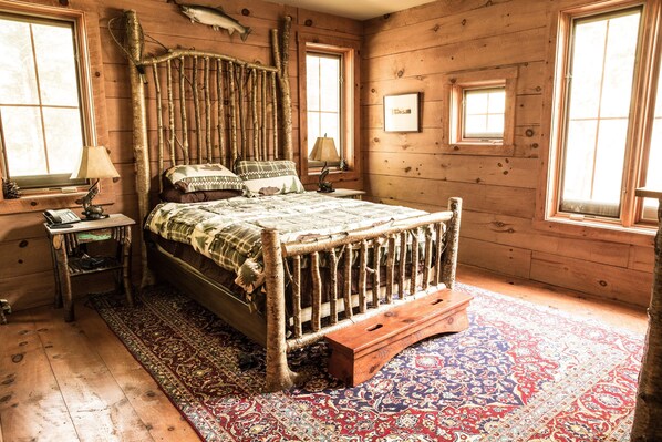 Una habitación rústica de madera con una cama con dosel, una alfombra estampada y una mesita con una lámpara.