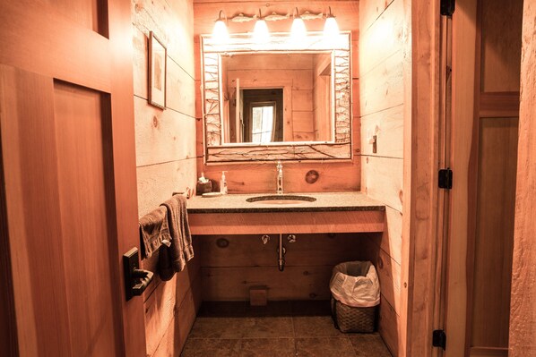 Un baño estrecho con paredes de madera, un lavabo, un espejo y un cubo de basura.