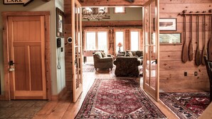 A wooden interior with a large door labeled "LAKE," a chandelier, and various hunting equipment.