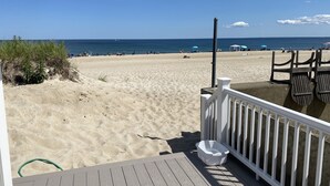 Ett trädäck med ett vitt räcke som vetter ut mot en sandstrand med parasoller och strandstolar.