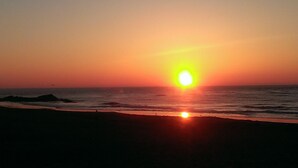 Un coucher de soleil sur l’océan, avec des vagues qui se brisent sur une plage.