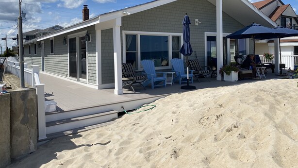 Ett hus vid stranden med en täckt uteplats, utomhusmöbler och utsikt över havet.