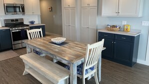 Une cuisine moderne avec des meubles blancs, des appareils en acier inoxydable et une table à manger en bois, assortie de chaises bleues.