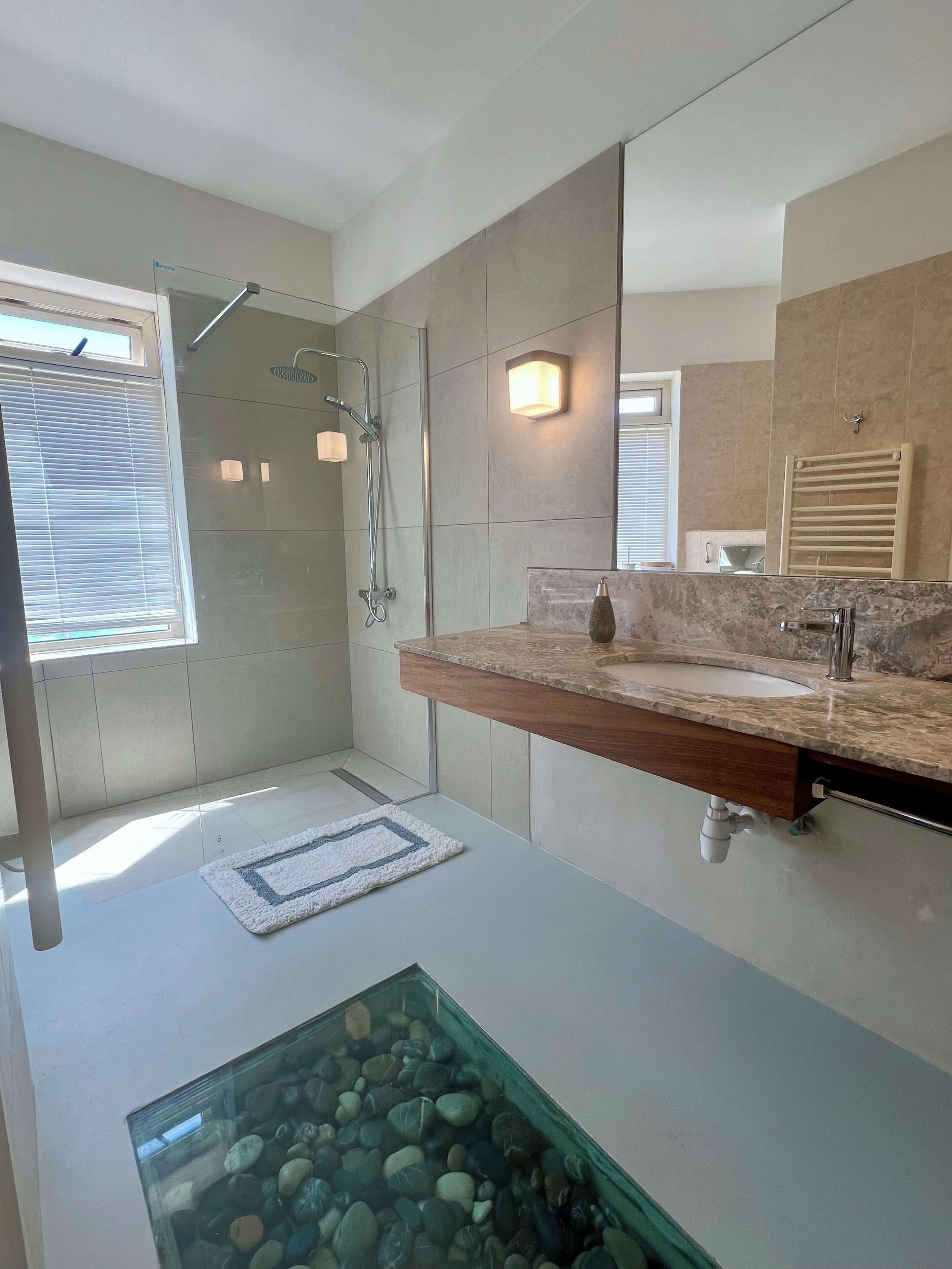 Une salle de bain moderne avec une douche à l’italienne, un grand miroir et un plan de toilette en marbre.