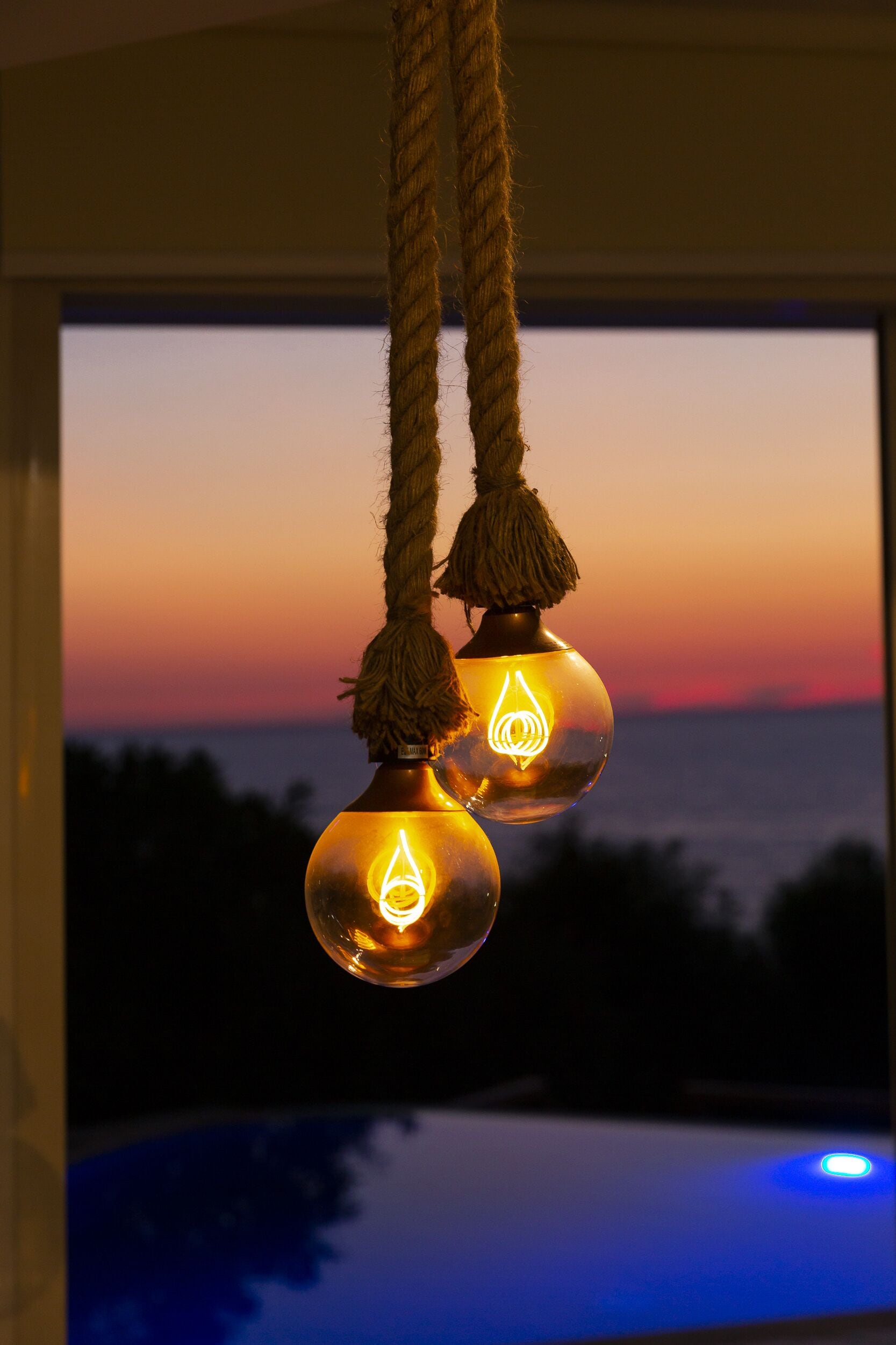 Deux luminaires sphériques suspendus, chacun contenant une ampoule visible, et maintenus en place par une corde.