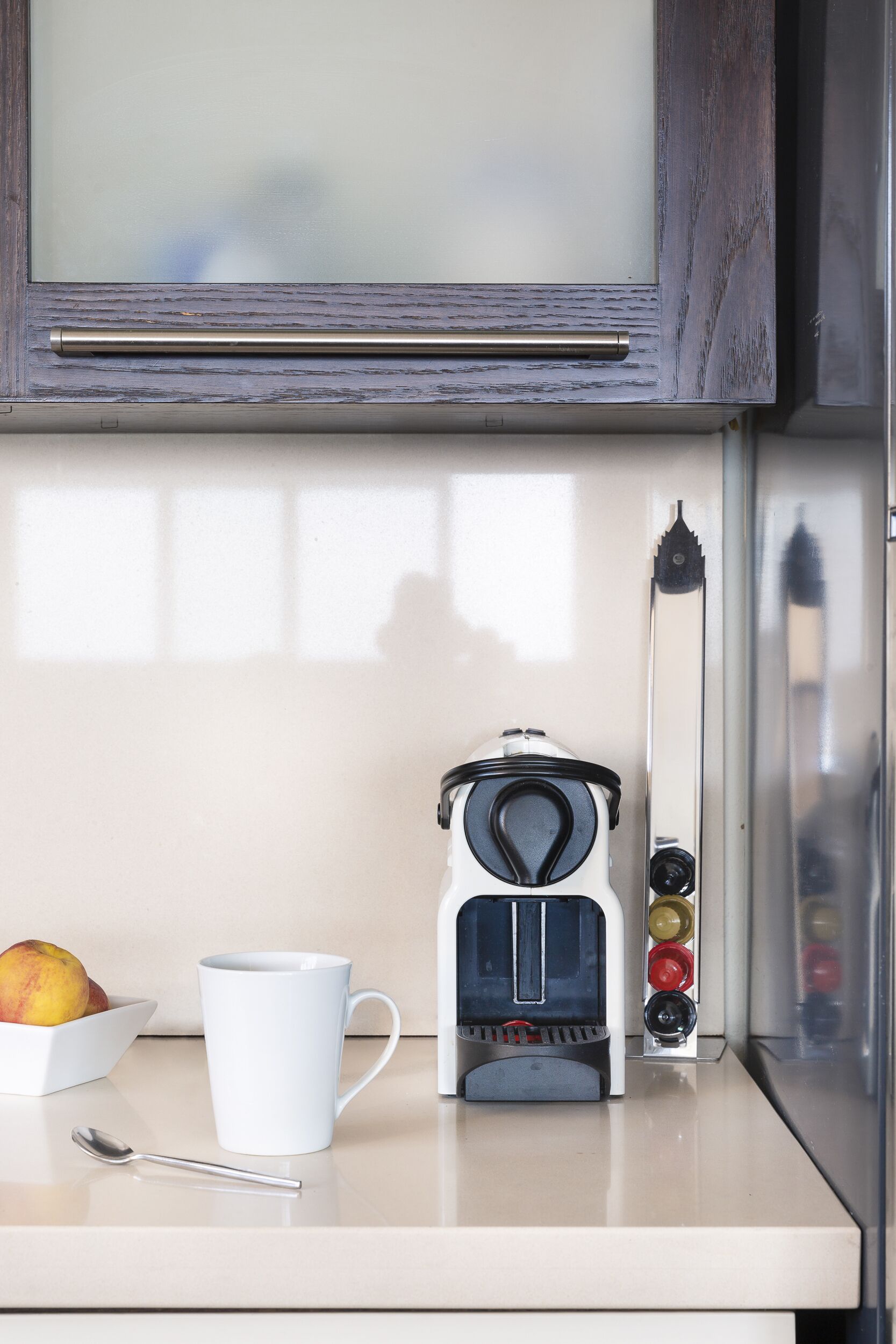 A kitchen with a coffee maker, a white mug, and a bowl of fruit on the counter.