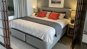 A modern bedroom with a large bed, grey and white bedding, two red pillows, a grey headboard, and a framed artwork above the bed. - Luxurious with great city views, free Private parking & fast internet  (South Yarra)