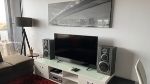 A modern living room with a flat-screen TV, two speakers, and a glass coffee table. - Luxurious with great city views, free Private parking & fast internet  (South Yarra)