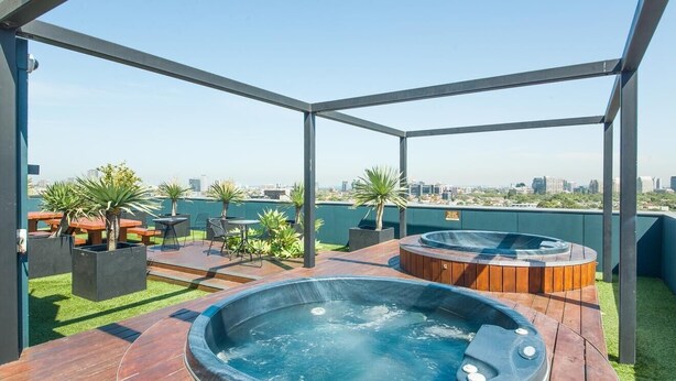 A rooftop patio with two hot tubs, outdoor seating, and a view of the city skyline. - Luxurious with great city views, free Private parking & fast internet  (South Yarra)