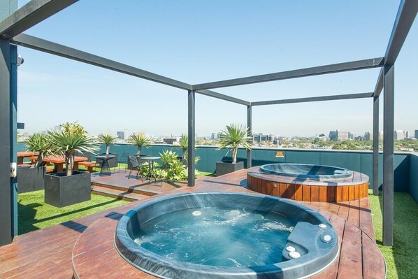 Enjoy a rooftop retreat with a city view, featuring two hot tubs and comfortable seating.