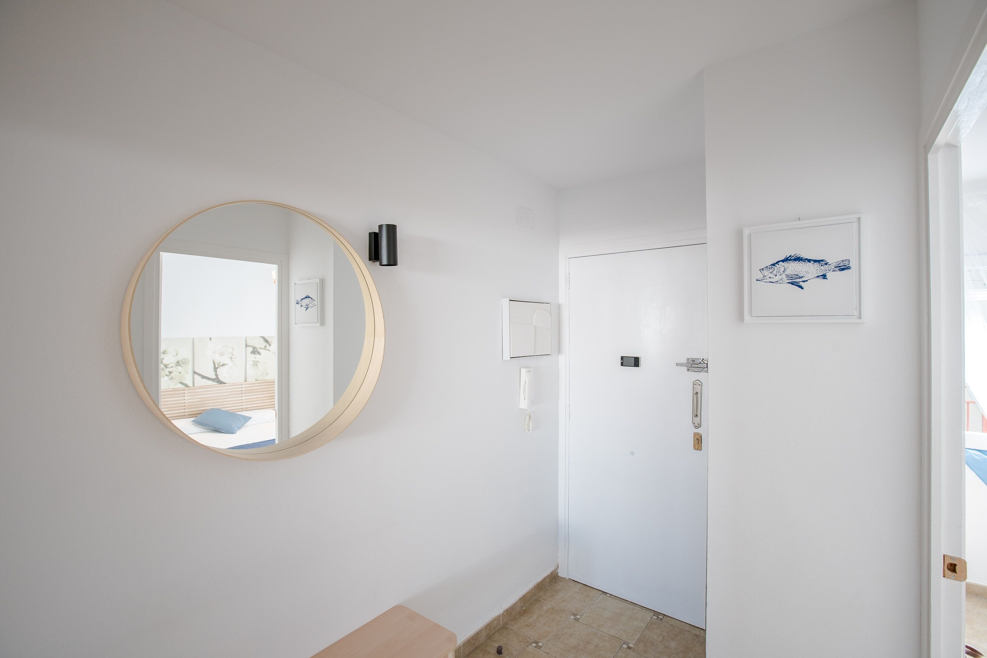 A hallway with a round mirror, a door, and a framed picture on the wall.