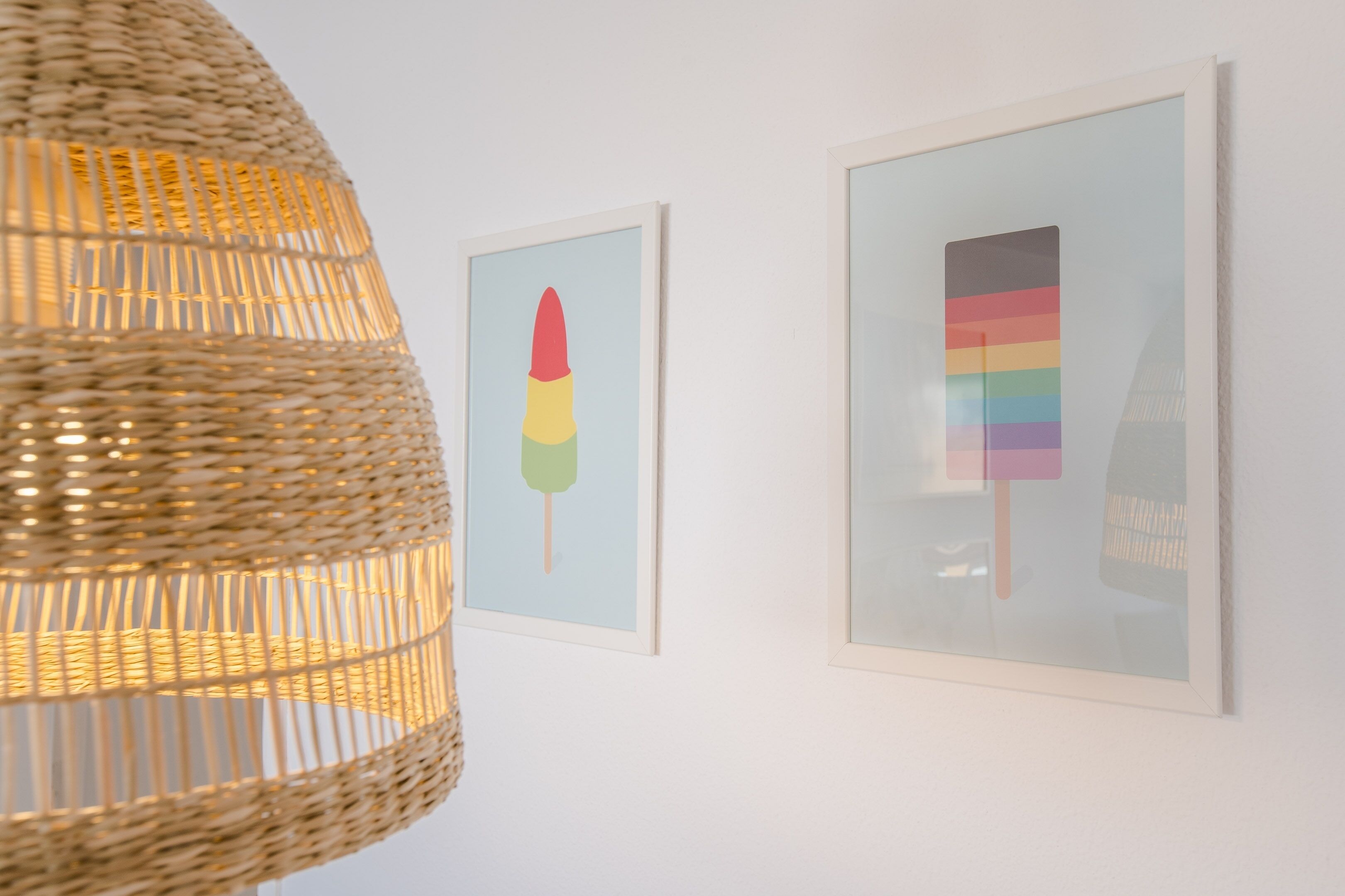 A wall with framed artwork and a woven light fixture.