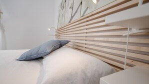 Une chambre à coucher moderne avec une tête de lit en bois, un lit simple avec une literie blanche et une table de chevet avec une lampe.