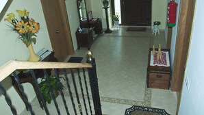 Una escalera con barandilla de madera, un jarrón de flores, un espejo, una mesita con una planta y un extintor en la pared.