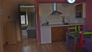 Cocina compacta con refrigerador, microondas y un lavamanos pequeño.  Comedor con sillas de colores y una mesa.