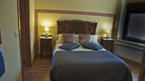 Una cama bien hecha con cabecera de madera, dos mesitas de noche con lámparas y vistas a una ventana con persianas.