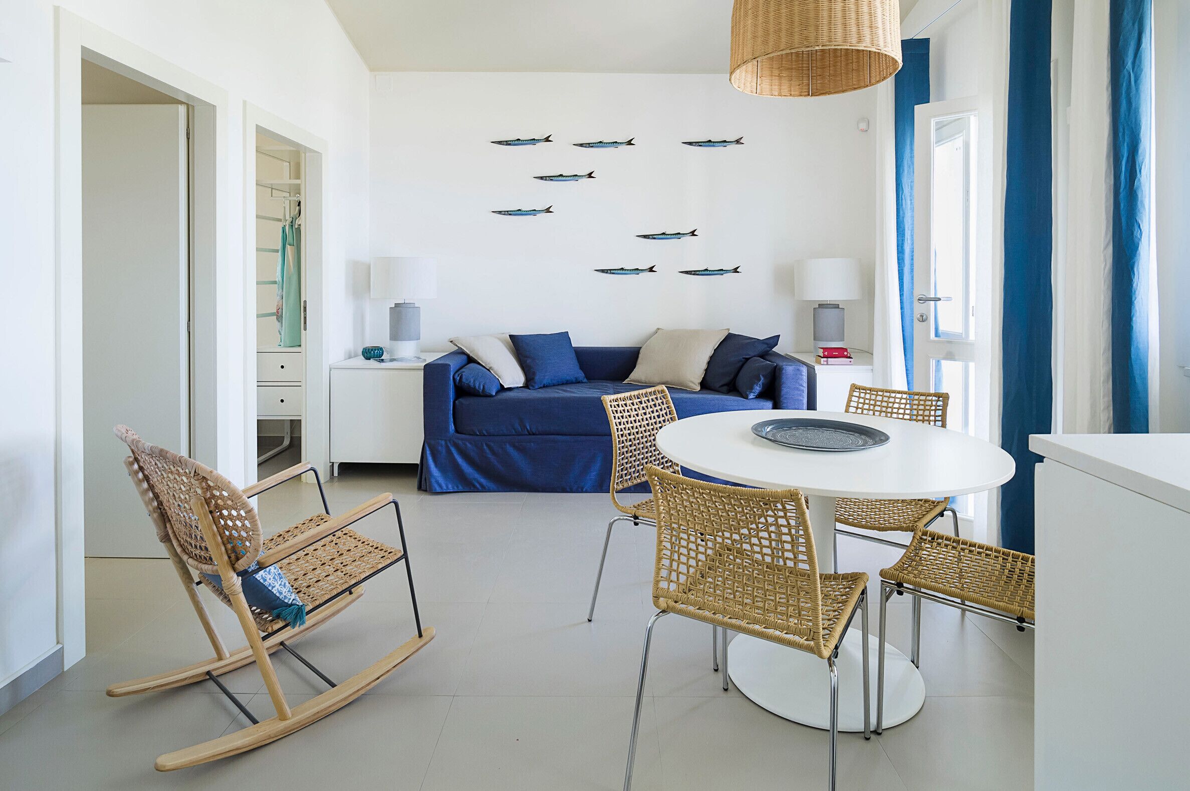 Uma sala de estar moderna com um sofá azul, móveis de vime e uma parede decorada com adesivos de peixes.