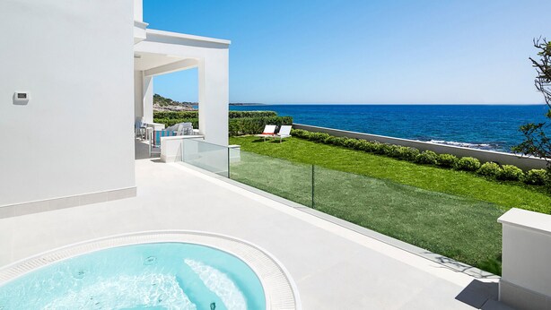 Un'area esterna moderna con vasca idromassaggio, ringhiera in vetro e vista sul mare.