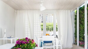 Una stanza luminosa e bianca con un tavolo e sedie, un soffitto bianco e vista sul verde circostante.