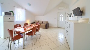 Eine moderne Küche mit Essbereich, weißen Schränken, einem Flachbildfernseher und einer gemütlichen Sitzecke mit Sofa und Kissen.