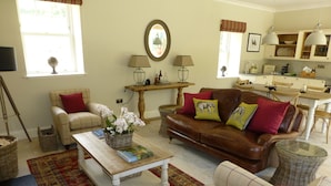 A living room with a brown leather sofa, a white armchair, and a coffee table with books and a vase of flowers. - Award Winning Ideal Rural Escape in Earn Valley 5 min from Perth (Perth)