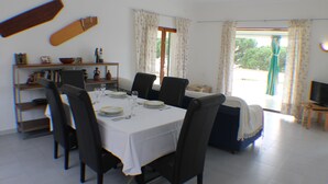 Een eethoek met een tafel voor vier personen, omringd door stoelen. Achtergrond toont een bank en een televisie.
