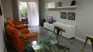 A modern living room with a glass dining table, orange sofas, a white entertainment unit, and a balcony with a view. - FULL CENTER REFURBISHED 6 SEATS WIFI. 3 MINUTES FROM LAUREL STREET WALKING (Logroño)