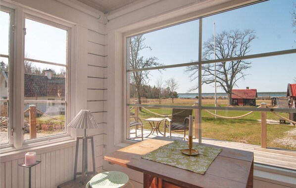 A room with a large window overlooking a grassy area and a body of water. There is a wooden table with a green tablecloth and a candle on a stand.