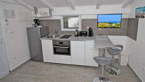 Une cuisine moderne équipée d’un four encastré, d’un évier et d’une machine à café. On y trouve une fenêtre avec des stores, un téléviseur fixé au mur et un tabouret de bar.