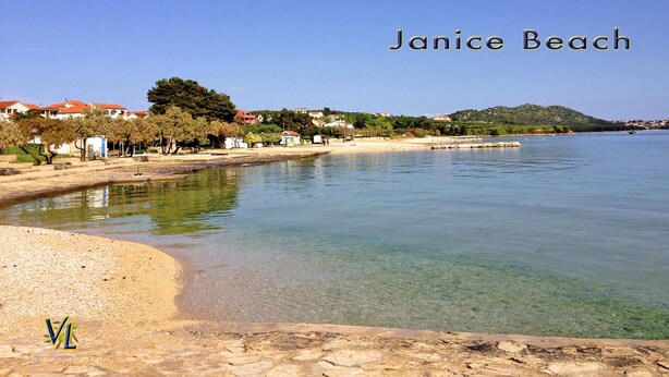 Janice Beach offre des eaux cristallines, une plage de sable et des maisons qui se dessinent à l’arrière-plan.