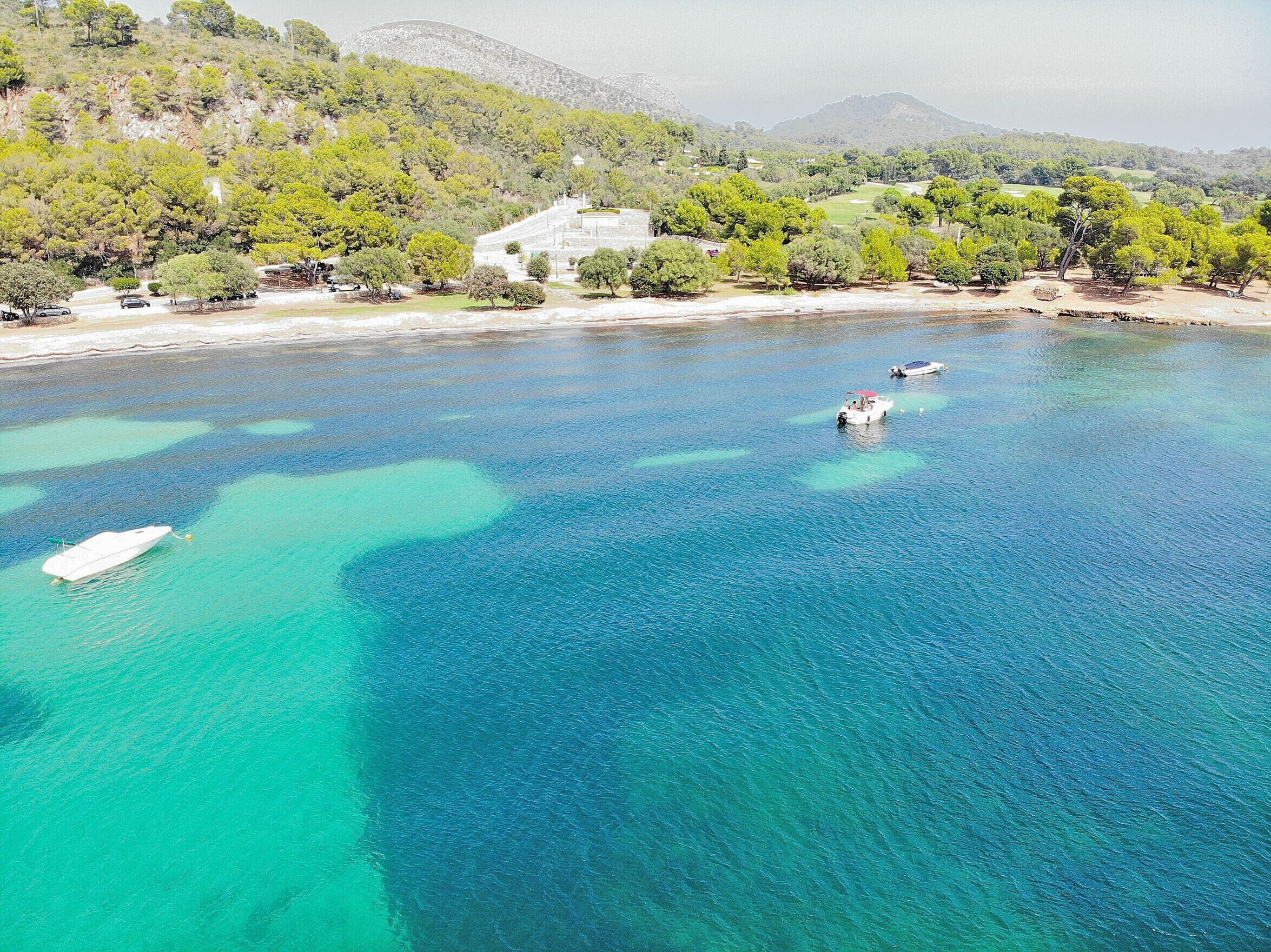 A coastal area with clear turquoise waters, boats, and a mountainous backdrop.