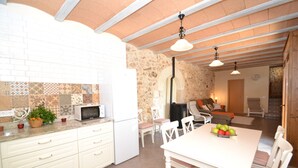 A kitchen with white cabinets, a microwave, and a dining area with a table and chairs. There is a stone wall and a wooden ceiling.