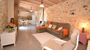 A cozy living room with a stone wall, a brown sofa with orange cushions, a white coffee table, and a small pink nightstand with a lamp.