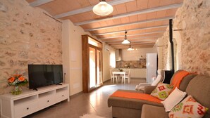 A cozy living room with a television, sofa, and decorative pillows. A dining area is visible in the background.