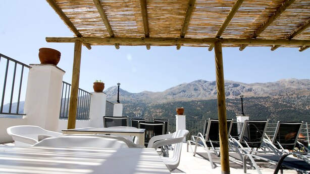 Una terrazza con sedie e tavoli bianchi, una pergola e vasi in terracotta.